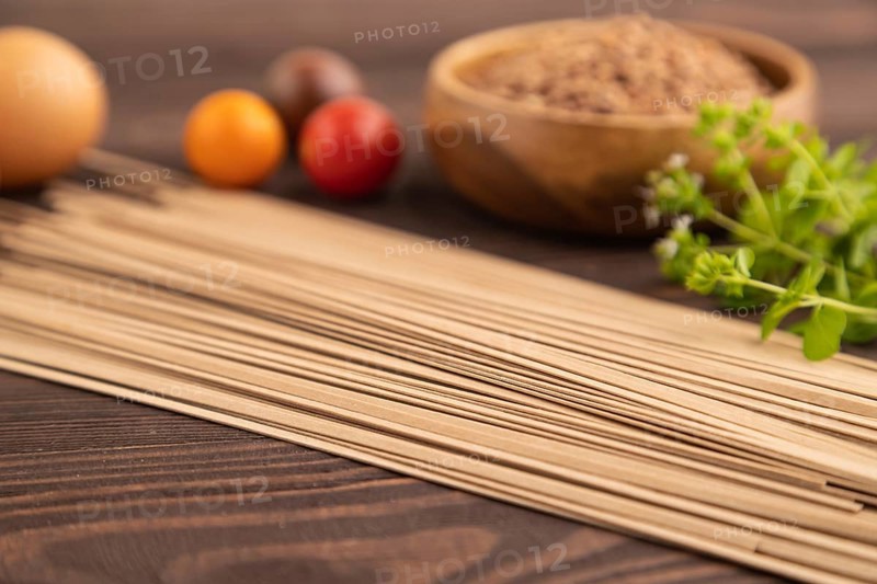 Japanese buckwheat soba noodles with tomato, eggs, spices, herbs on brown wooden background. Side view, close up, selective focus