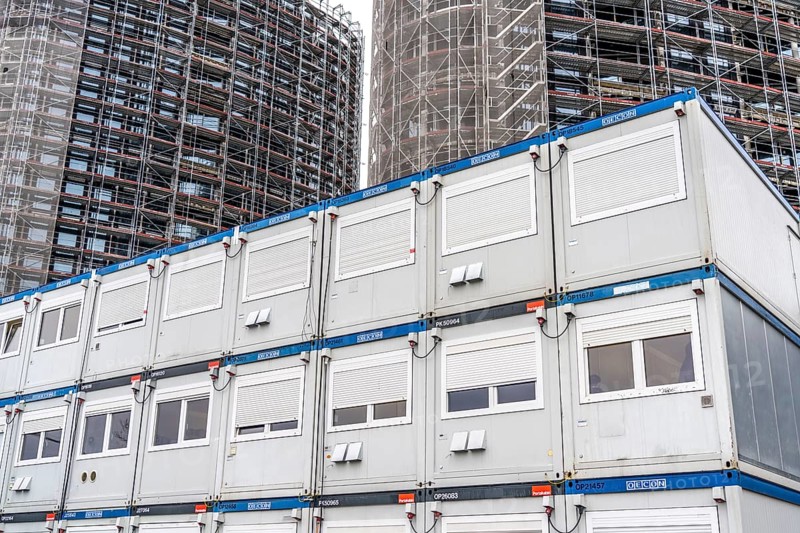 Large construction site, construction of a high-rise residential building, scaffolded shell, already fitted with windows, in front of it containers for offices, accommodation, washrooms, storage, for the construction workers