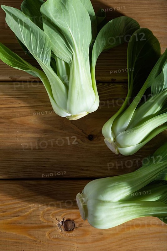 Fresh green bok choy or pac choi chinese cabbage on a brown wooden background. Hard light, contrast. Top view, close up, flat lay