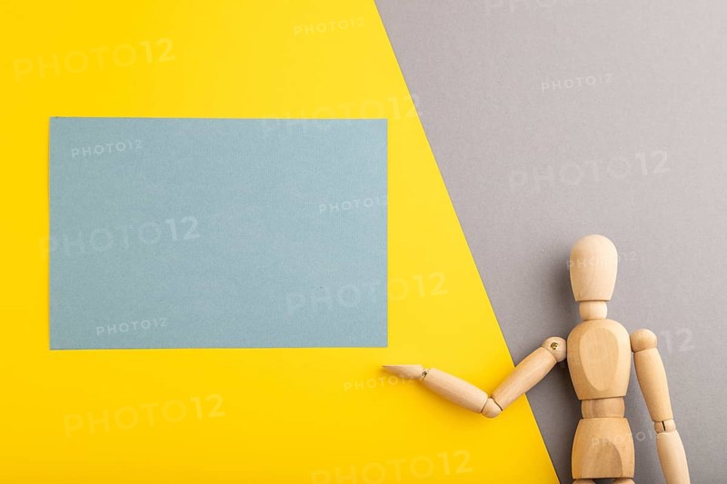 Wooden mannequin holding blue blank poster on gray and yellow pastel background. copy space, isolated, presentation concept, trendy colors