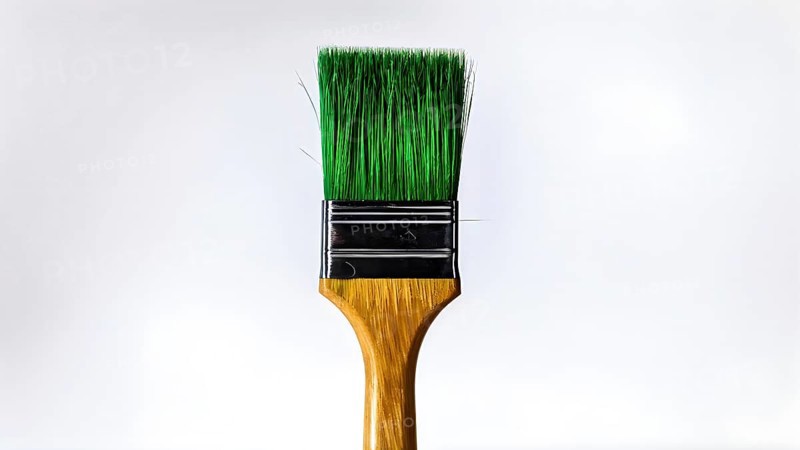 Thick paintbrush dipped in green bristles dripping onto a white background, AI generated