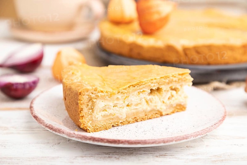 Autumn onion pie and cup of coffee on white wooden background and linen textile. Side view, close up, selective focus