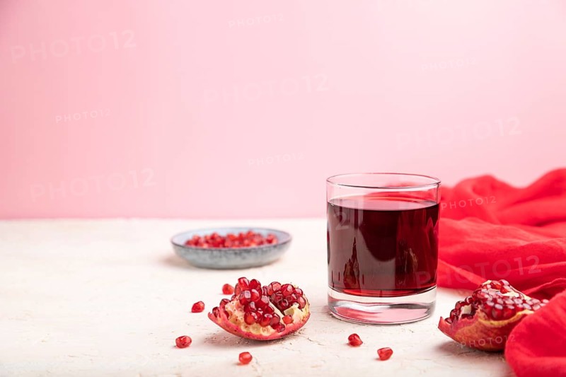 Glass of pomegranate juice on a white and pink background with red textile. Side view, copy space, selective focus