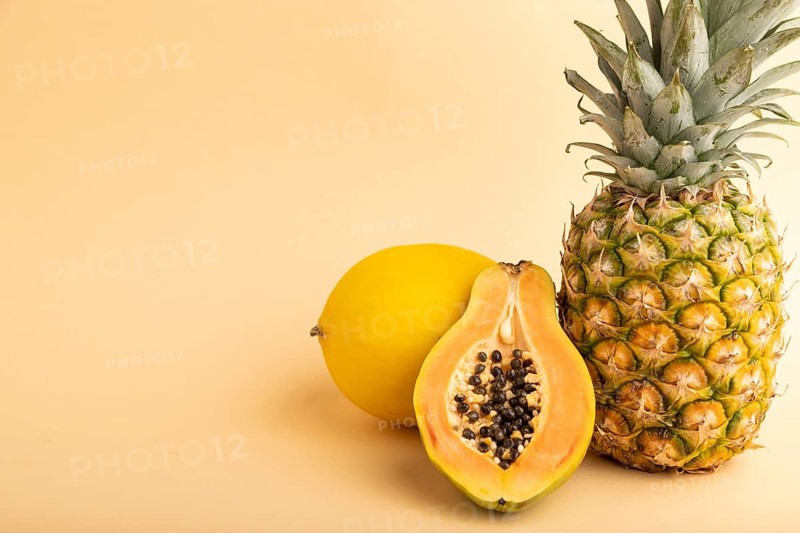 Ripe cut papaya, pineapple, melon, on orange pastel background. Side view, copy space. Tropical, healthy food, vacation, holidays concept