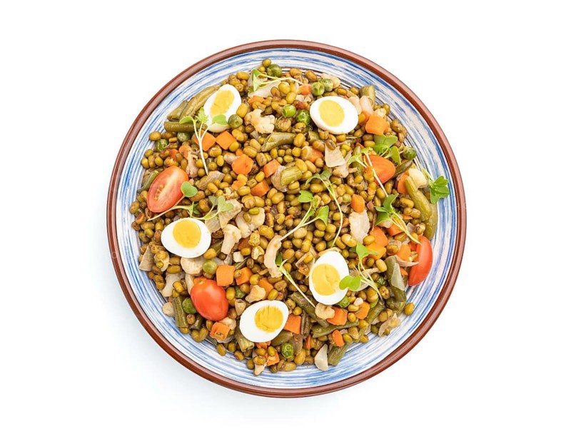 Mung bean porridge with quail eggs, tomatoes and microgreen sprouts isolated on a white background. Top view, close up