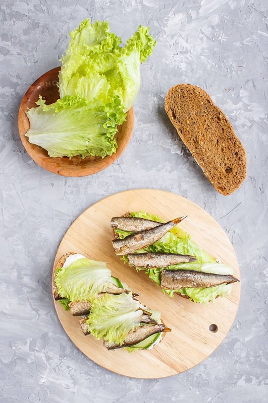 Sprats sandwiches with lettuce and cream cheese on wooden board on a gray concrete background. top view, flat lay