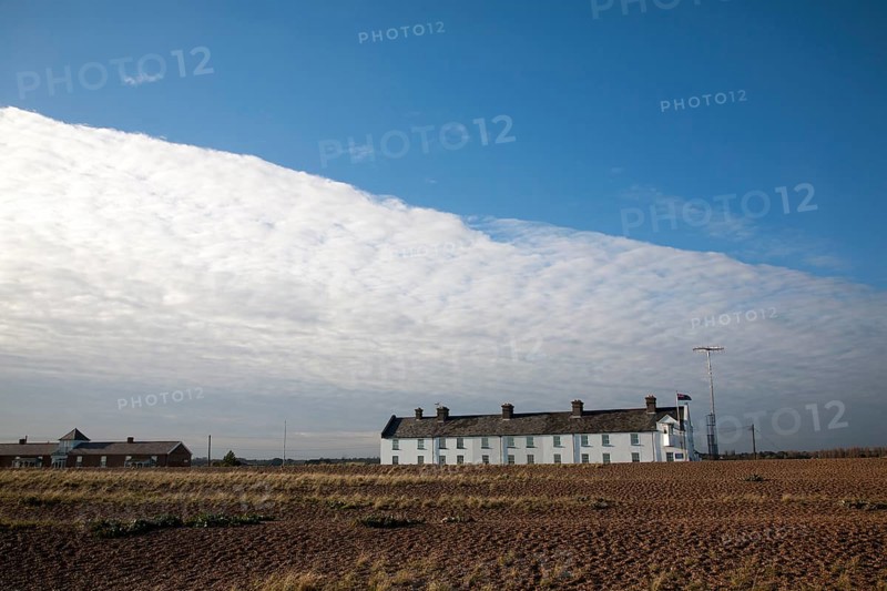 Frontal clouds passing over Coastguard Cottages shingle beach at Shingle Street, Suffolk, England, UK
