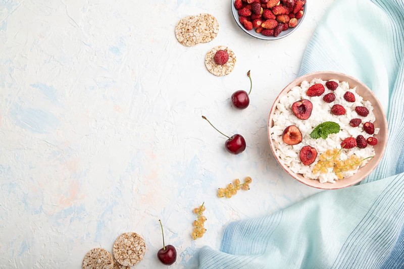 Rice flakes porridge with milk and strawberry in ceramic bowl on white concrete background and blue linen textile. Top view, flat lay, copy space