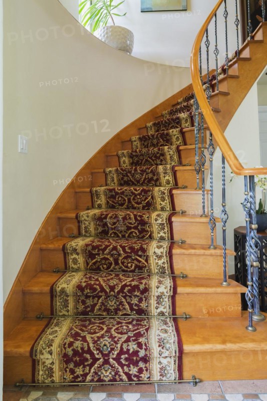 Wooden spiraling staircase with burgundy and cream coloured rug runner and brass rods leading to upstairs inside a luxurious residential home, Quebec, Canada, North America