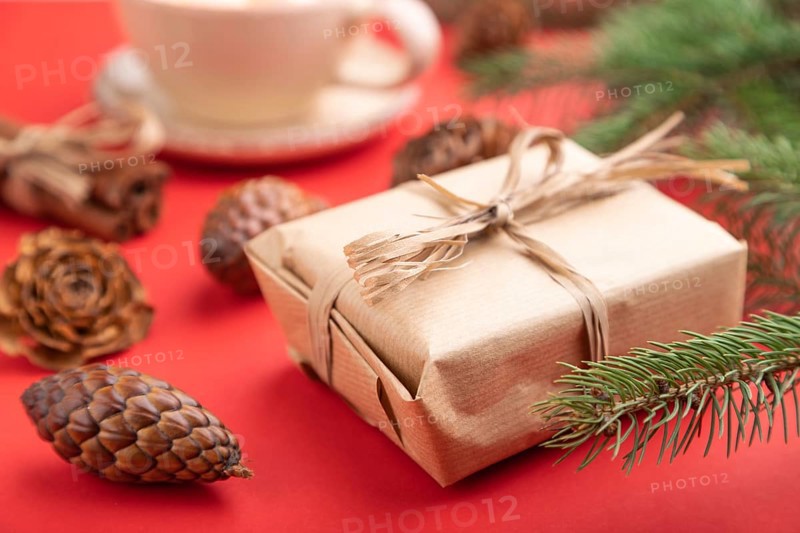 Christmas or New Year composition. Decorations, box, cinnamon, cones, fir and spruce branches, cup of coffee, on a red paper background. Side view, close up, selective focus