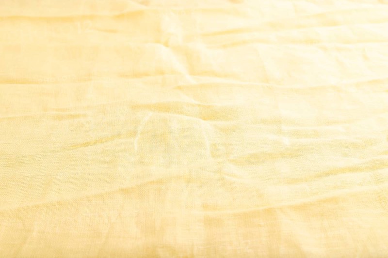 Fragment of smooth yellow linen tissue. Side view, natural textile background and texture