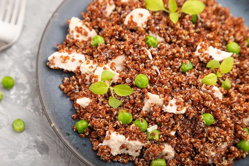 Quinoa porridge with green pea and chicken on ceramic plate on a gray concrete background and orange textile. Top view, close up, selective focus