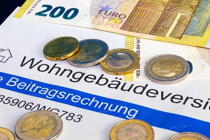 Symbolic image of building insurance: close-up of contract documents, a model house, euro banknotes and euro coins