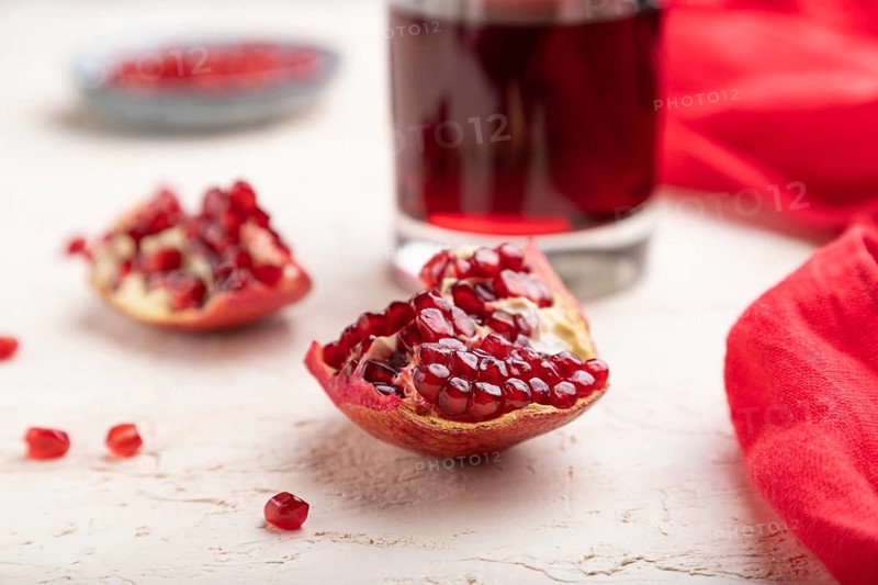 Glass of pomegranate juice on a white concrete background with red textile. Side view, close up, selective focus