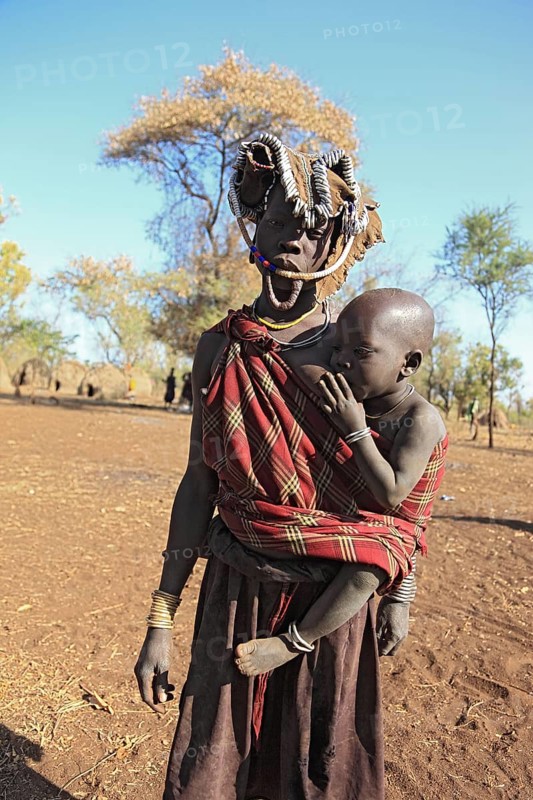 South Ethiopia, in Maco National Park, Mursi tribe, Mursi woman with baby, painted skin and headdress, baby drinking from breast, plate-lipped woman without plate, Ethiopia, Africa