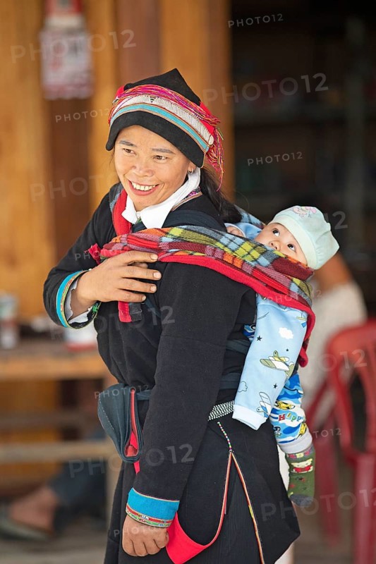Vietnamese woman, 43 years old, in traditional traditional costume of the Dao minority, carrying her son, 3 months, on her back, Nam Dam Dao Cultural Village, Ha Giang province, Vietnam, Asia