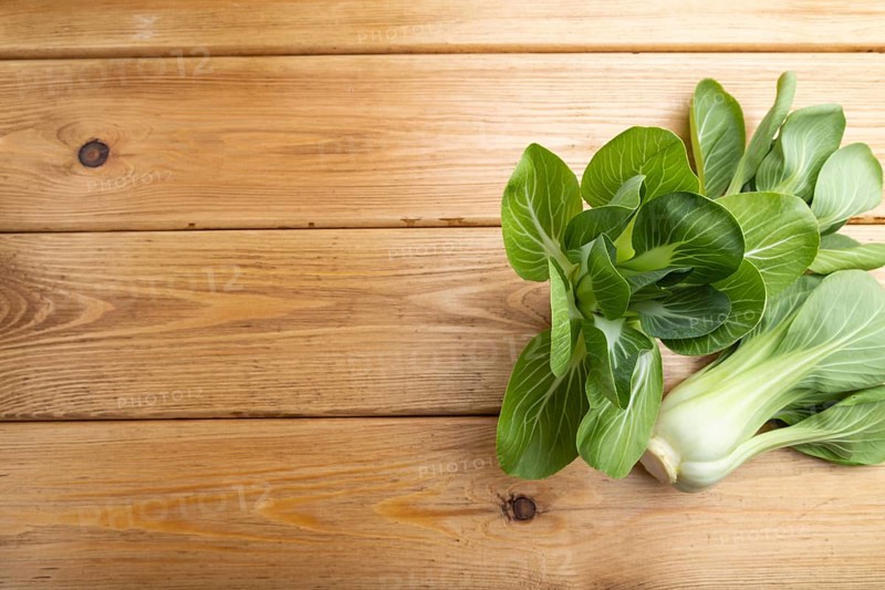 Fresh green bok choy or pac choi chinese cabbage on a brown wooden background. Top view, copy space, flat lay