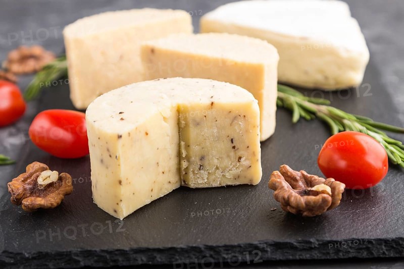 Cheddar cheese and various types of cheese with rosemary and tomatoes on black slate board on a black concrete background. Side view, close up, selective focus