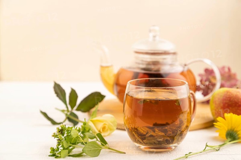 Red tea with herbs in glass teapot on white wooden background. Healthy drink concept. Top view, close up, selective focus
