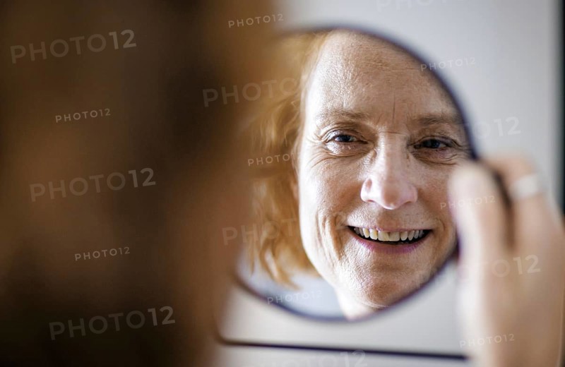 Symbol photo. A smiling elderly woman can be seen in a mirror. Berlin, 13.08.2024