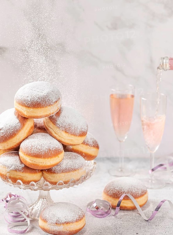 Doughnuts on a glass stand, rosé sparkling wine is poured in the background, falling icing sugar