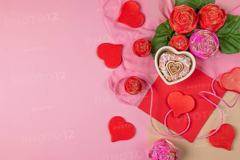 An arrangement of decorative hearts, roses and an envelope, heart-shaped cupcake, ideal for Valentine's Day, on a pink background