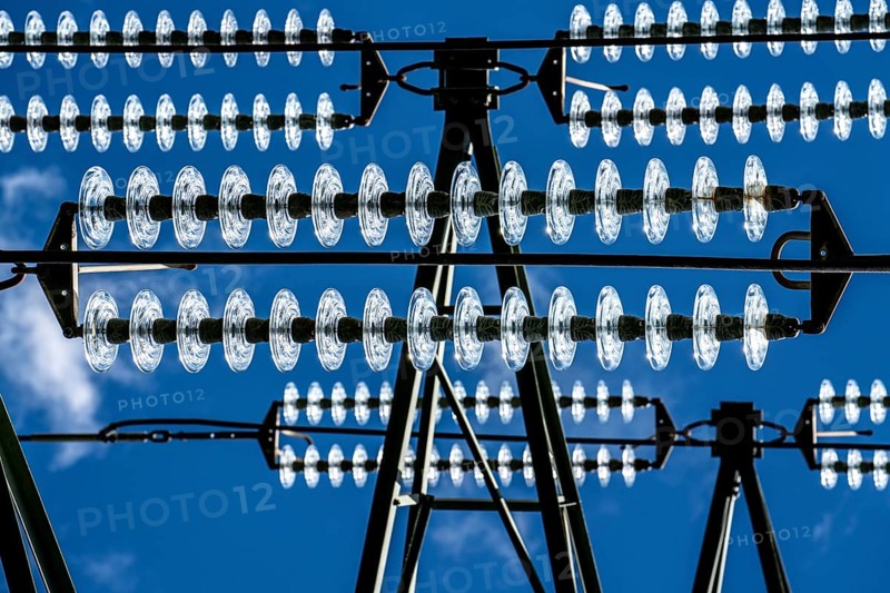 Insulators made of glass on a high-voltage line, they hang on the pylons as a suspension device between the pylon and the live, non-insulated cable, extra-high voltage line, symbolic image energy