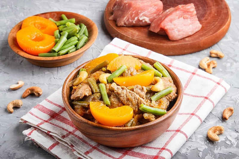 Fried pork with peaches, cashew and green beans on a black concrete background. side view, close up, flat lay, chinese cuisine. linen textile