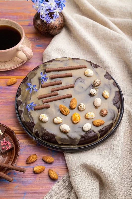 Homemade chocolate brownie cake with caramel cream and almonds with cup of coffee on a colored wooden background and linen textile. Side view, close up
