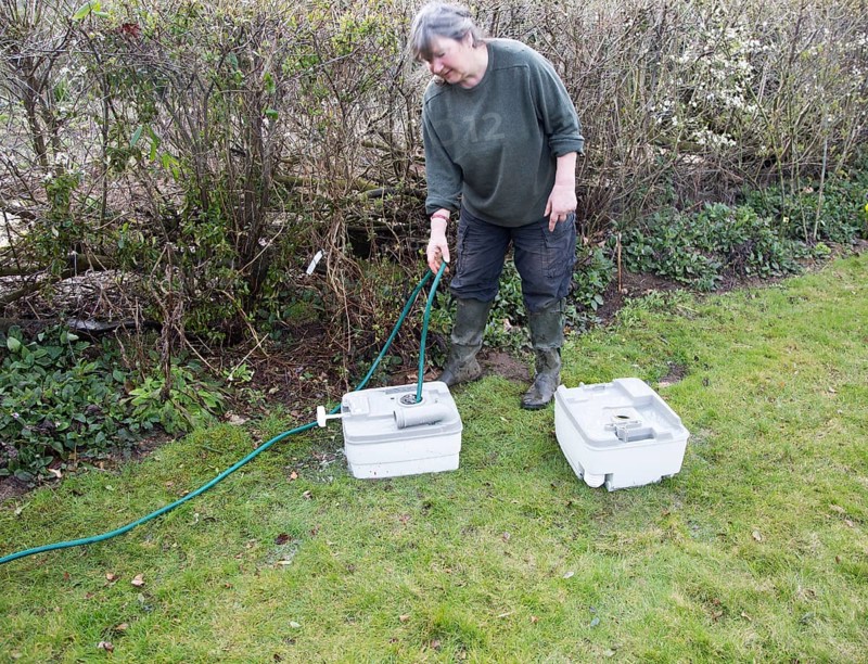Woman using garden hose water pipe to wash clean camping toilet container cartridge, UK