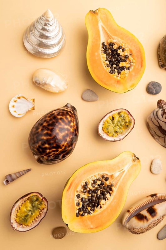 Ripe cut papaya, passion fruit, seashells, pebbles on orange pastel background. Top view, flat lay, close up. Tropical, healthy food, vacation, holidays concept