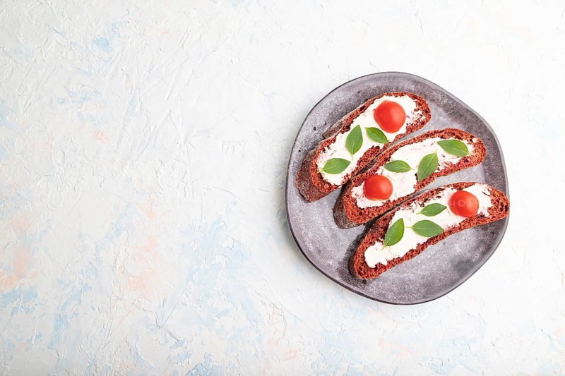 Red beet bread sandwiches with cream cheese and tomatoes on white concrete background. top view, flat lay, copy space