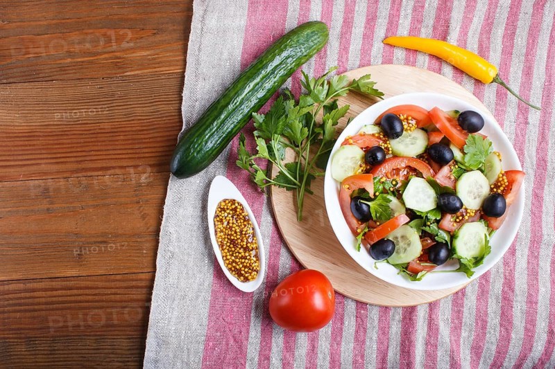 Vegetarian salad of tomatoes, cucumbers, parsley, olives and mustard on linen tablecloth, top view, flat lay, copy space