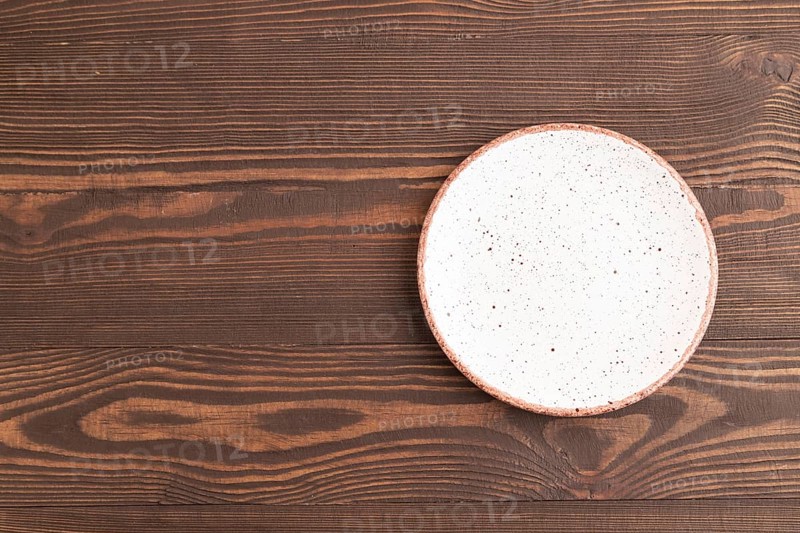 Empty white with dots ceramic plate on brown wooden background. Top view, copy space, flat lay
