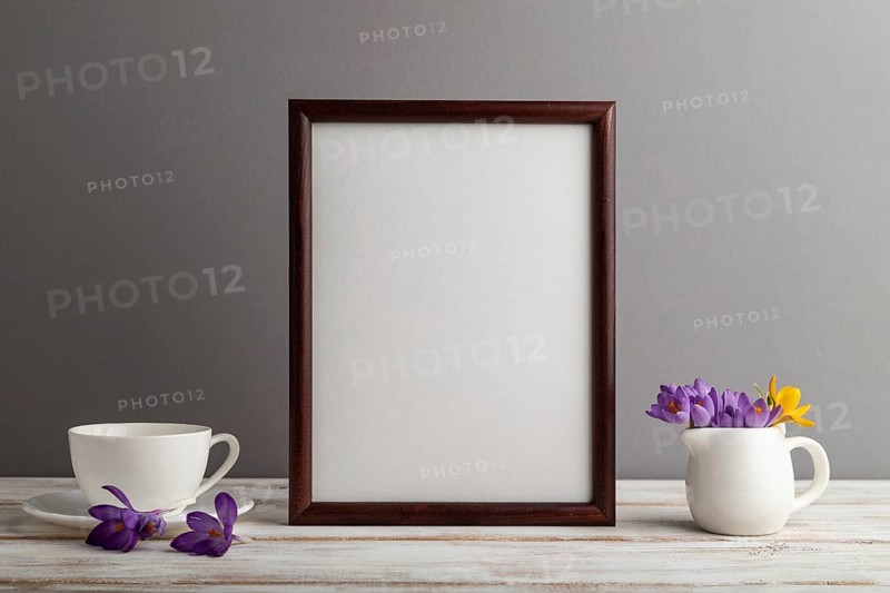 Brown wooden frame mockup with snowdrop crocus flowers and white coffee cup on gray paper background. Blank, vertical orientation, still life, copy space