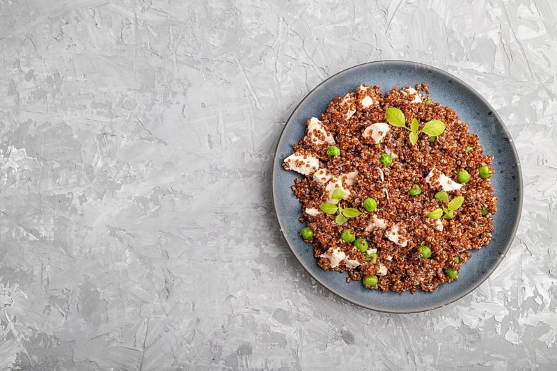 Quinoa porridge with green pea and chicken on ceramic plate on a gray concrete background. Top view, flat lay, copy space