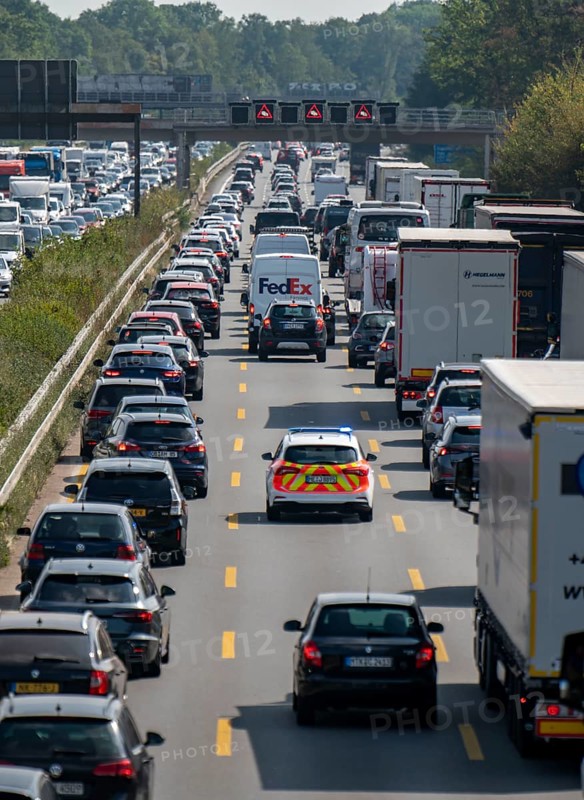 Emergency ambulance with flashing blue lights and siren working its way through a traffic jam on the A3 motorway, over 8 lanes, in both directions, in front of the Leverkusen motorway junction looking north, Friday afternoon heavy traffic, delays due to the traffic jam, Leverkusen, North Rhine-Westphalia, Germany, Europe