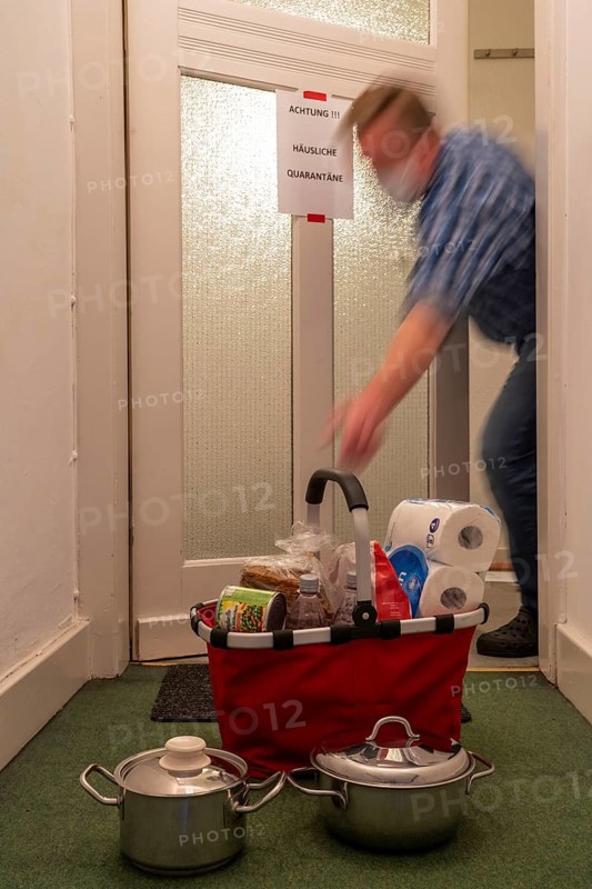 Symbolic image Domestic quarantine, man is in isolation at home due to a suspected corona infection, warning sign for visitors on the front door, communicates with a visitor through the door, neighbours have been shopping, cooked and put the things in front of the door