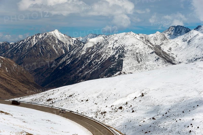Verschneite Berge und eine kurvenreiche Straße in einer winterlichen Landschaft in Andorra, nördlich von El Pas de la Casa, Pyrénées-Orientales, Encamp, Fürstentum Andorra, Pyrenäen