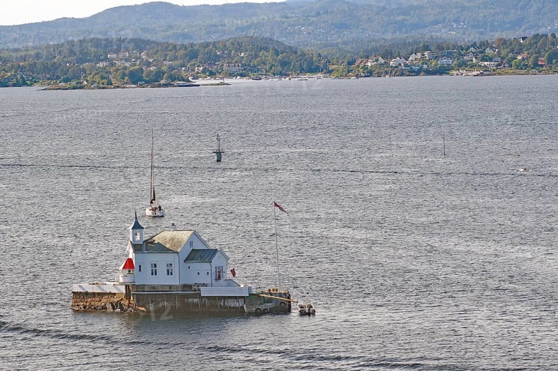 A lighthouse, restaurant in the sea with a small sailing boat and a hilly landscape in the background, Dyna Fyr, Oslofjord, capital city, Oslo, Norway, Europe