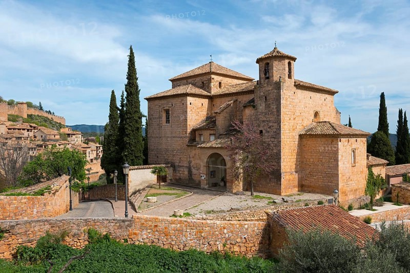 A medieval stone church surrounded by cypress trees in a tranquil Mediterranean landscape under a blue sky, Parish Church of San Miguel, Alquézar, Alquezar, Huesca, Aragón, Aragon, Pyrenees, Spain, Europe