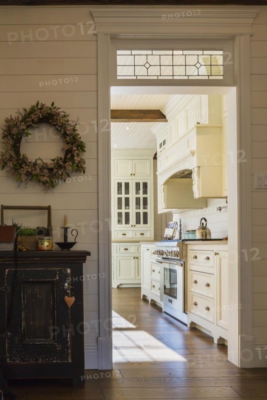 White painted maple wood antique style cabinets with tan coloured quartz countertops in kitchen with stained oak wood floorboards inside country style home, Quebec, Canada, North America