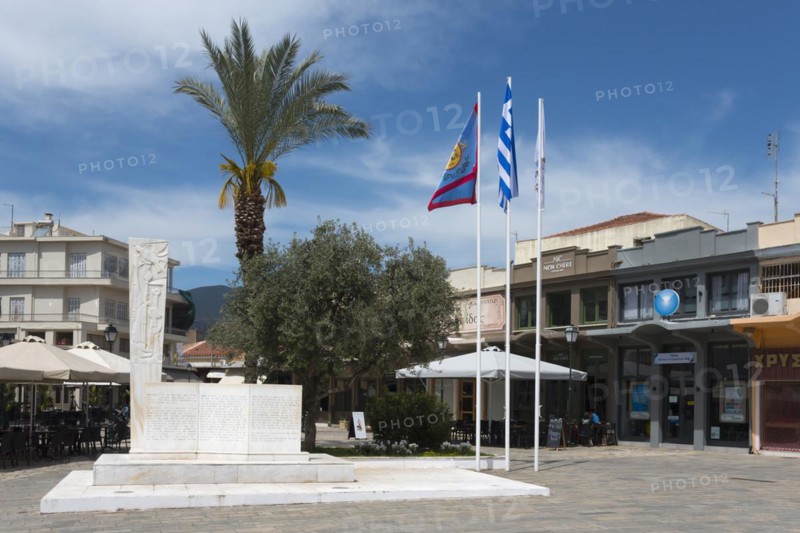 A town square with a monument surrounded by palm trees, flags and a café, 23 March Square with a monument commemorating the beginning of the struggle for freedom, Kalamata, Messinia, Peloponnese, Greece, Europe