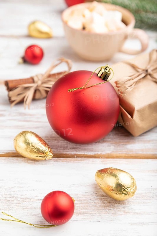 Christmas or New Year composition. Decorations, box, red balls, cinnamon, fir and spruce branches, cup of coffee, on a white wooden background. Side view, close up, selective focus