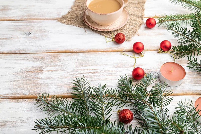 Christmas or New Year composition. Decorations, red balls, fir and spruce branches, cup of coffee, candles on a white wooden background. Side view, copy space