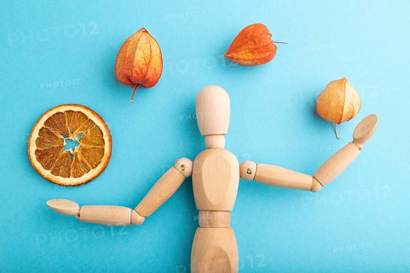 Wooden mannequin juggling dried citrus and physalis on blue pastel background. close up, isolated