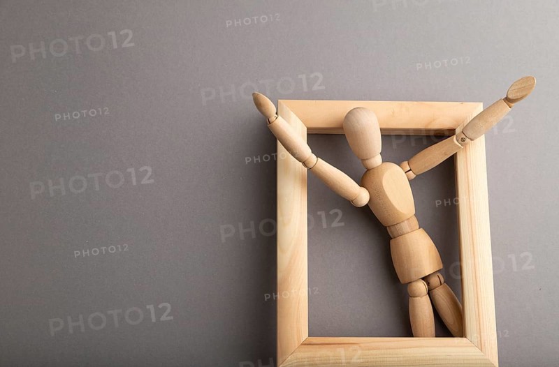 Wooden mannequin climbs out of a wooden frame with raised arms on gray pastel background. escape, break rules, freedom, welcome, greeting, joy concept. copy space