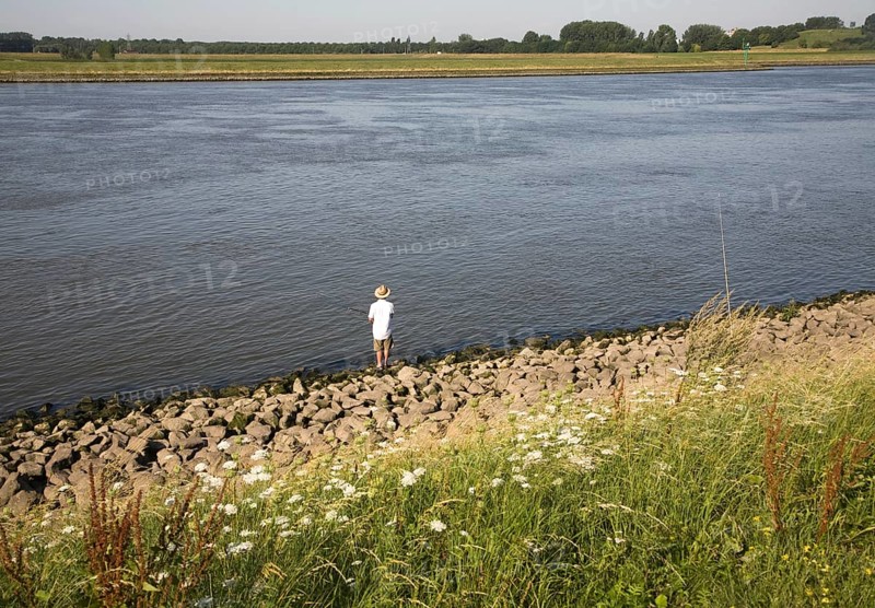 Man standing alone fishing in River Maas, Ablasserdam, Netherlands