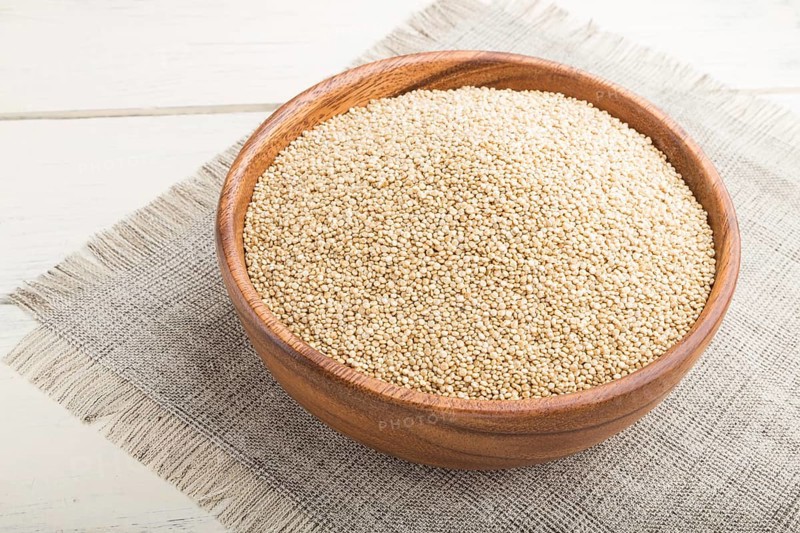Wooden bowl with raw white quinoa seeds on a white wooden background and linen textile. Side view, close up