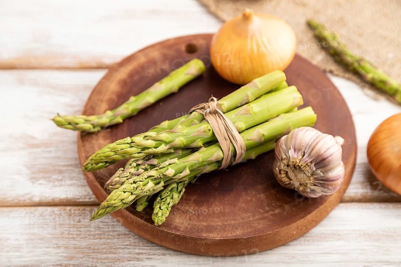Bunch of fresh green asparagus, garlic, onion on white wooden background. Side view, selective focus. harvest, healthy, vegan food, concept